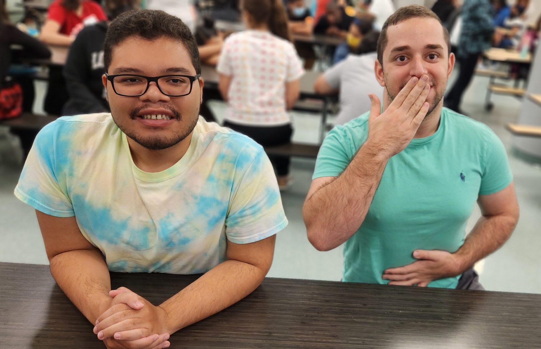 Two male students sitting in the school cafeteria together.