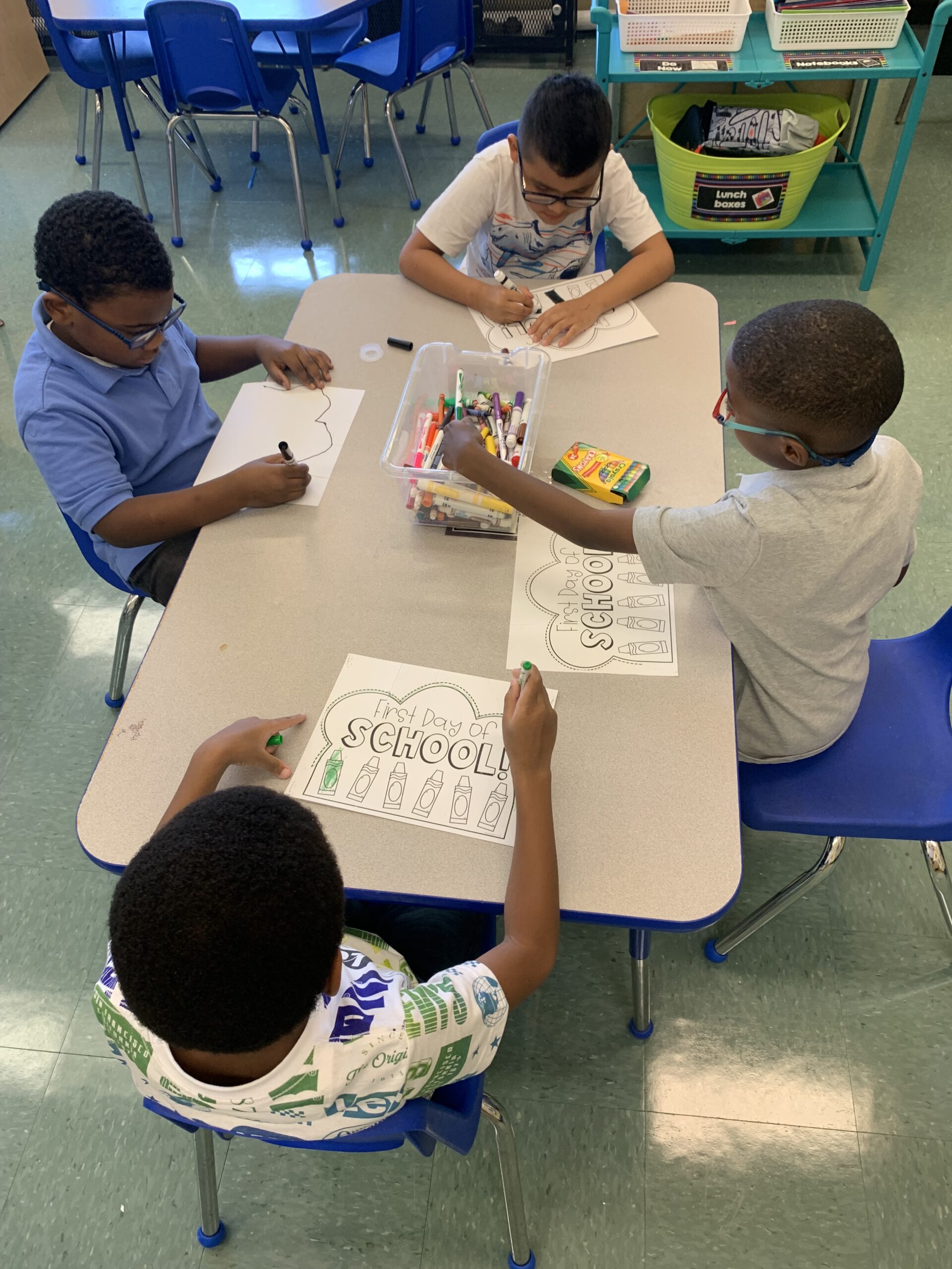 Four students using markers to complete their work at their desk.