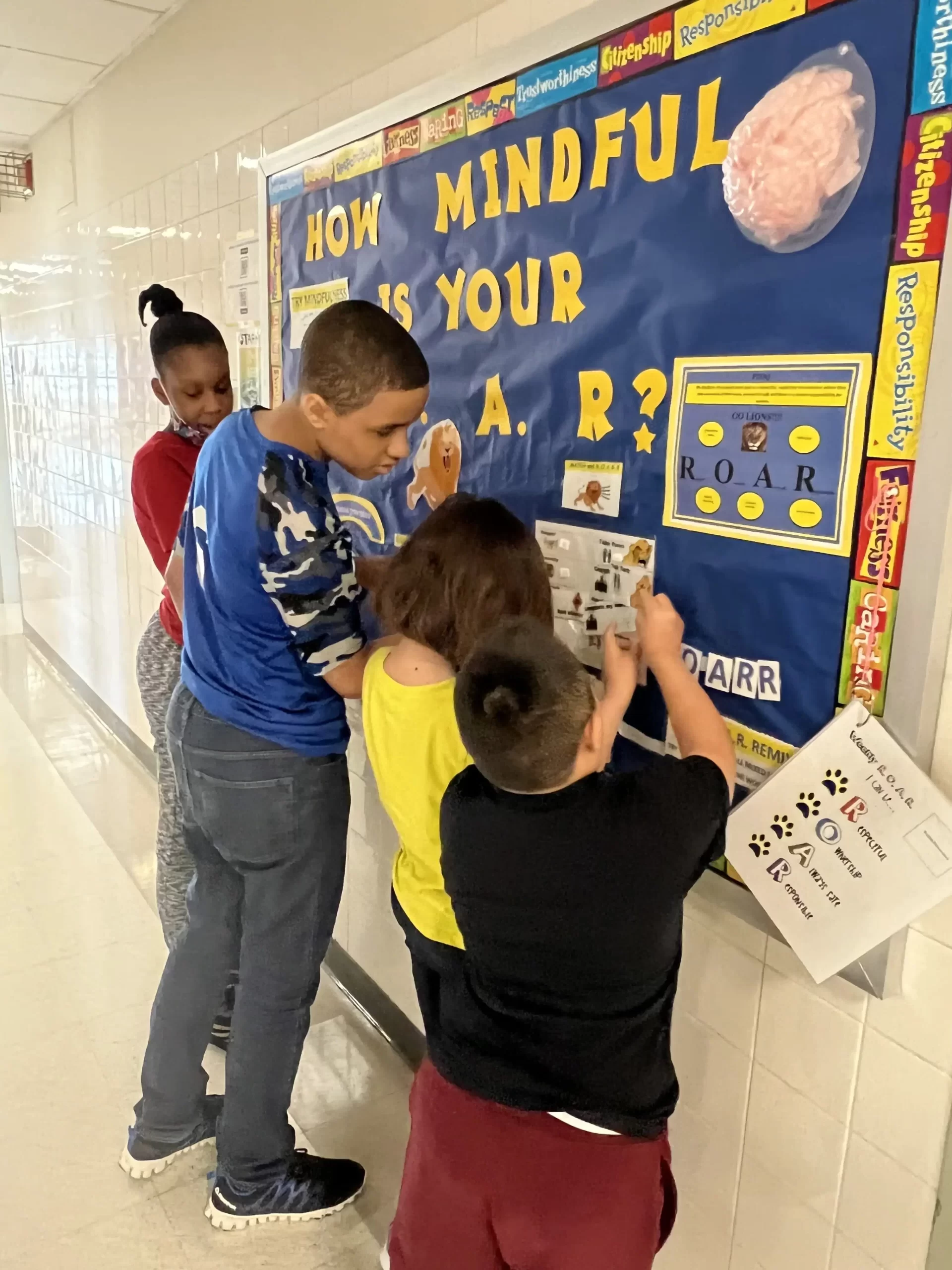 Two girls and two boys putting pictures on a bulletin board called how mindful is your roar?