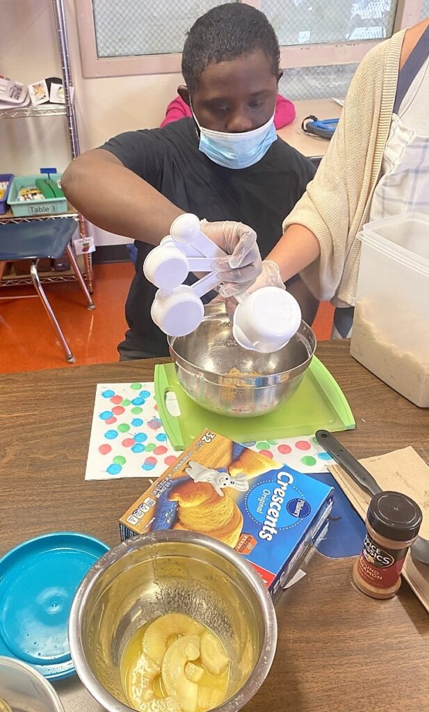 male student using measuring cups to pour a cake mixture into a bowl