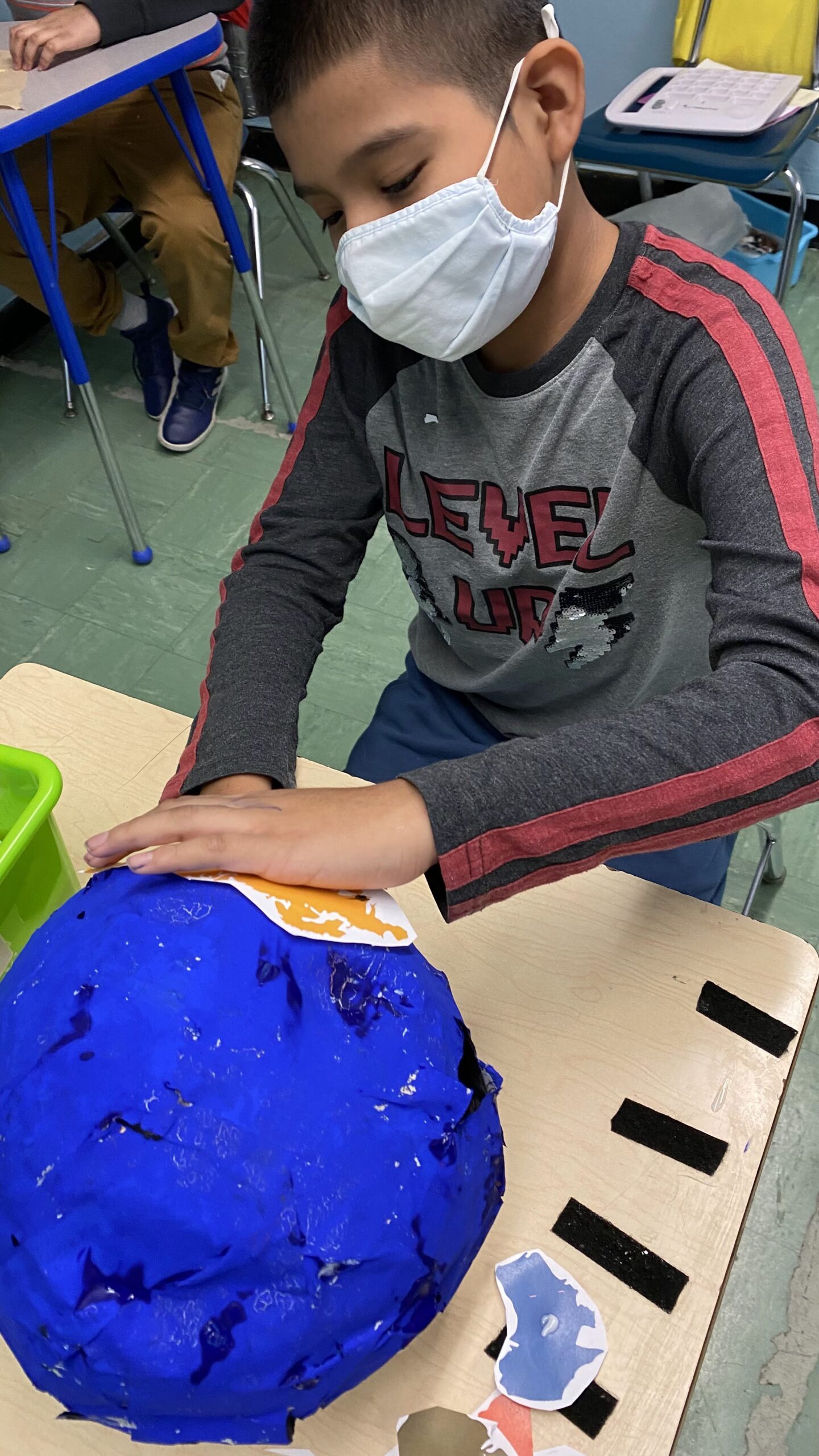 male student in a grey shirt with red stripes on the sleeve pasting pictures of the brain sections onto a brain model.