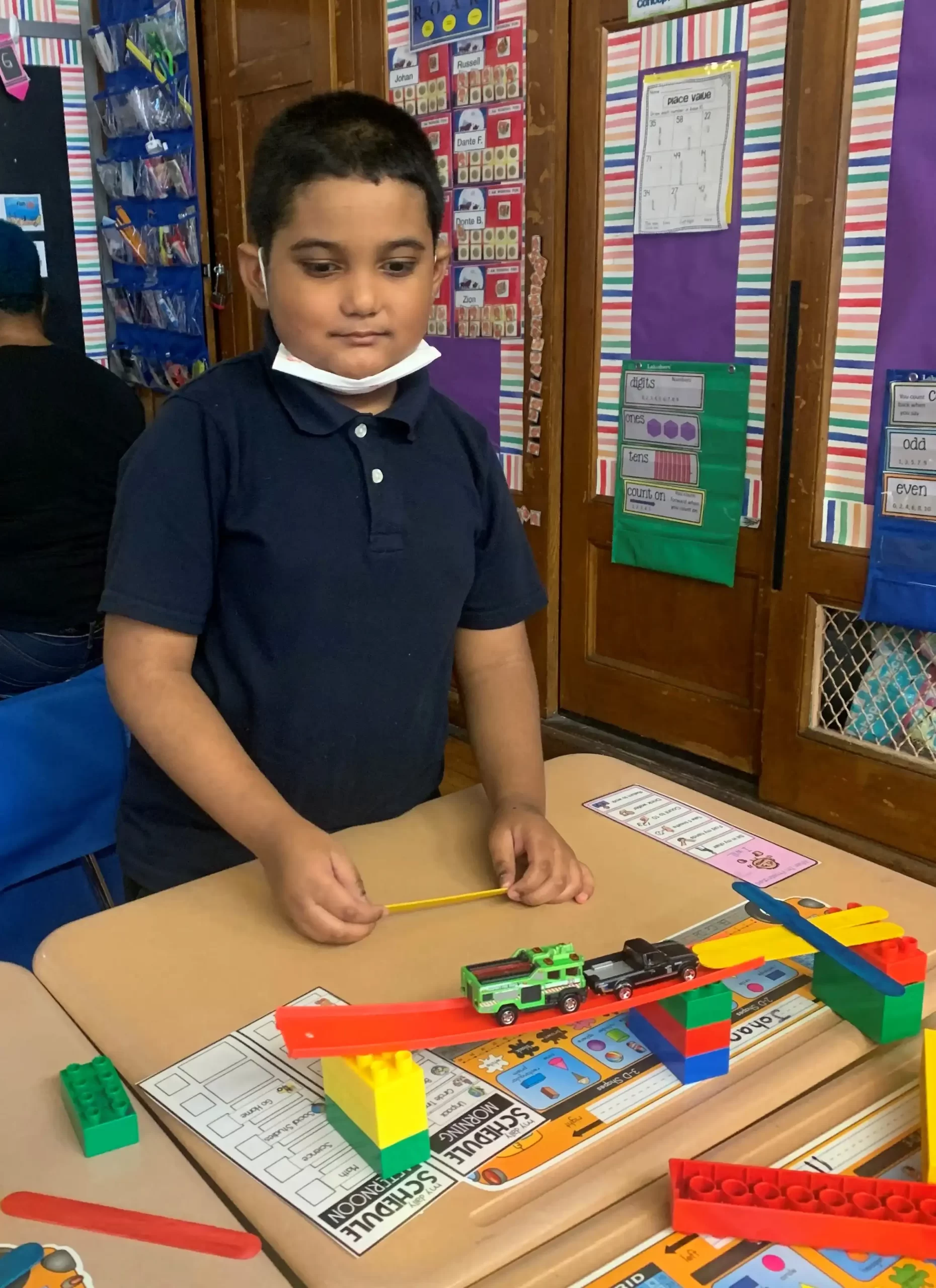 boy with a blue shirt using blocks and a toy car to build a bridge.