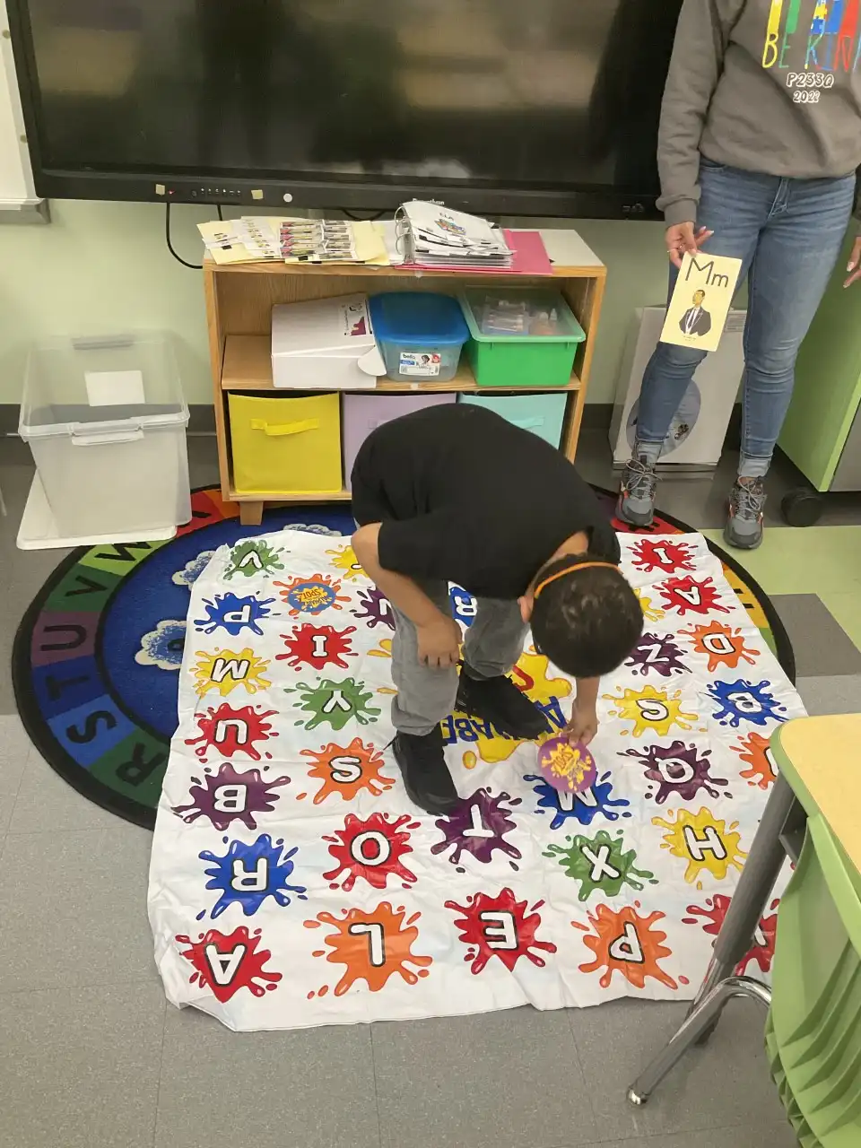 boy staning on a mat with different colored letters of the alphabet matching numbers and colors using cards.