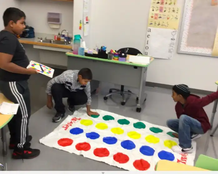 three male students working together as they play a game on a mat with different colored circles.
