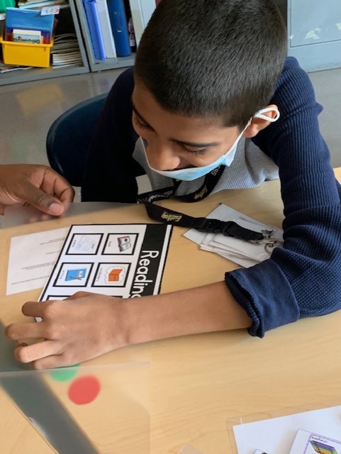 student wearing a blue shirt pointing to a picture to answer a question posed by a teacher