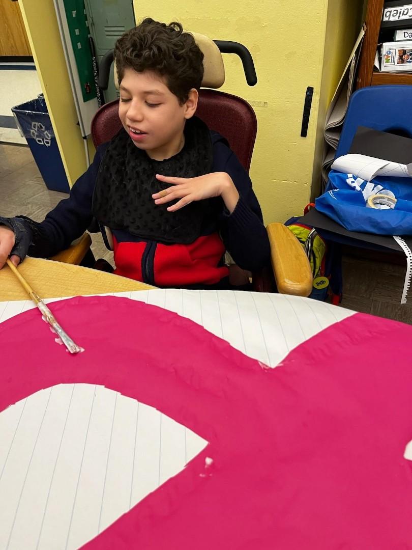 A student in a wheelchair using a paintbrush to create a pink ribbon