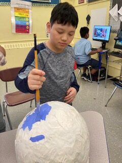 A student using a paintbrush on white ball