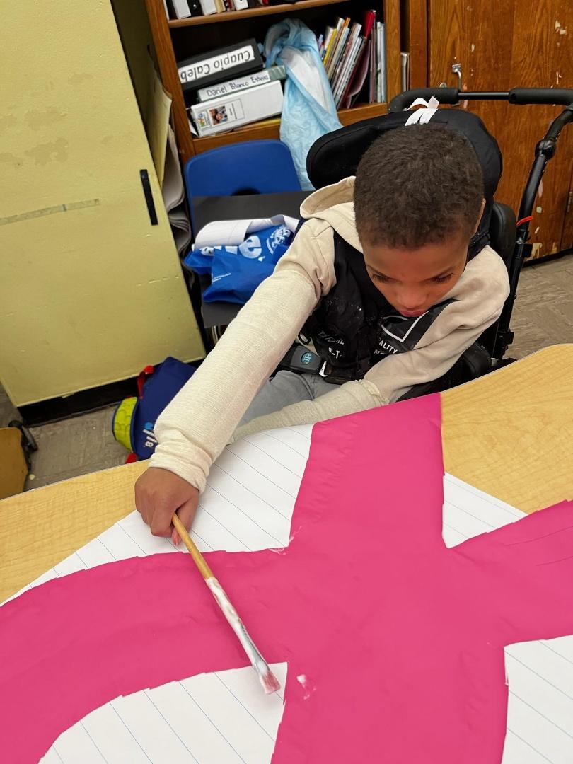 A student in a wheelchair using a paintbrush to create a pink ribbon
