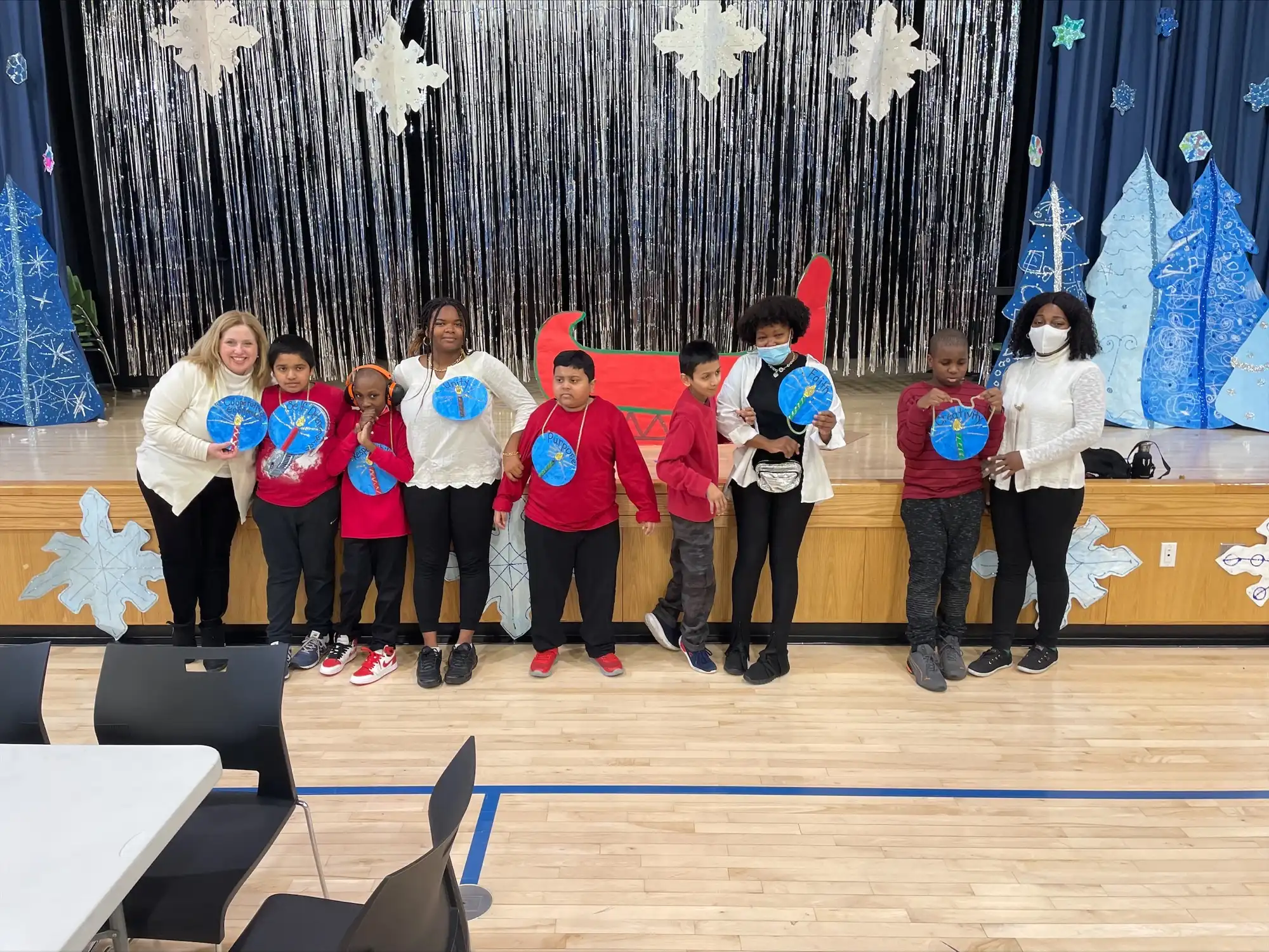 Five students and four teachers standing besides a stage decoratged with a winter theme.