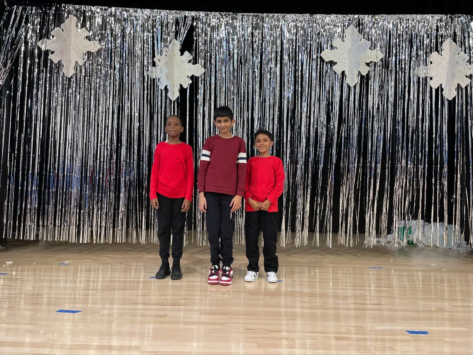Three male students wearing red on stage in their school audotorium.