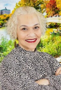 woman with blonde hair smiling with a lake and boats in the background.