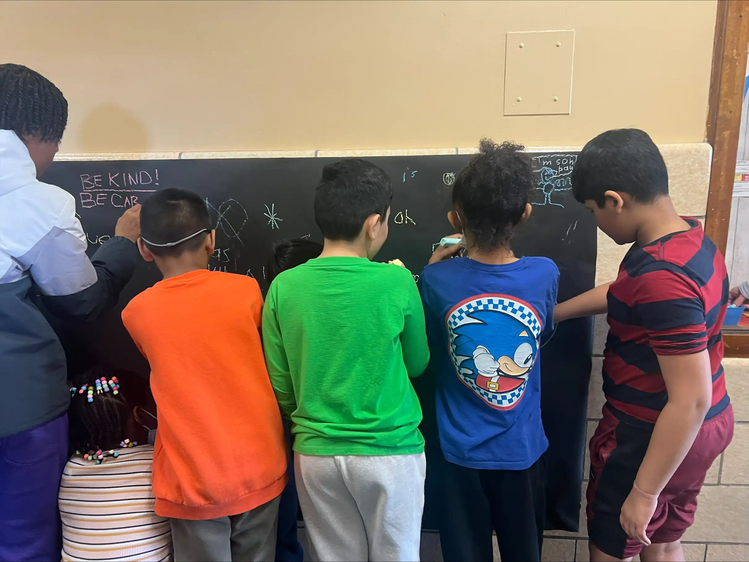 Five students drawing positive messages on a chalk board