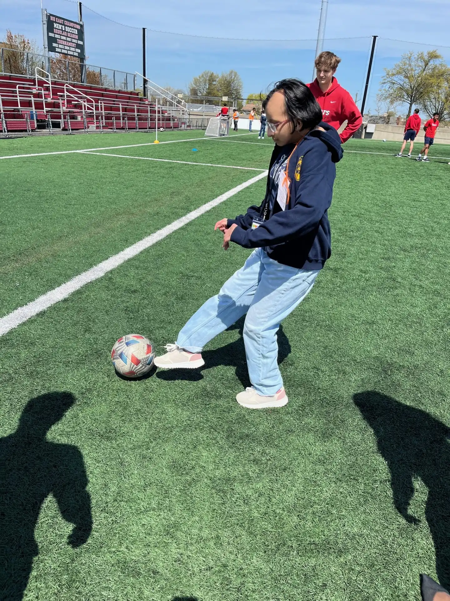 "A student in regular clothes is on a grassy field, kicking a ball."