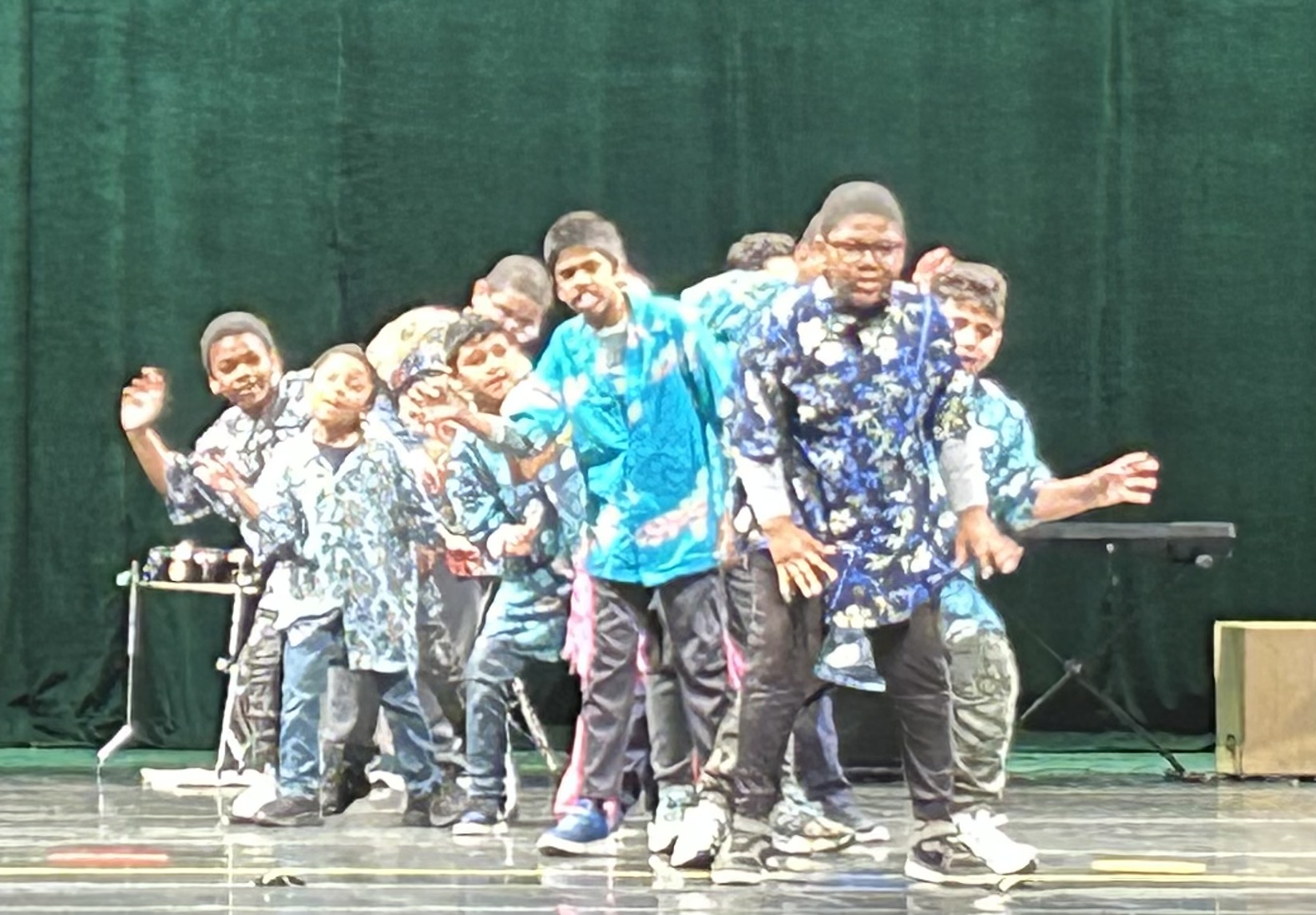 Elementary school students dancing on stage with a green background