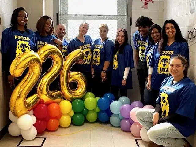 “A group of students and teachers stand together smiling in front of large yellow balloon numbers that read ‘226,’ with colorful balloons arranged beneath the numbers.”