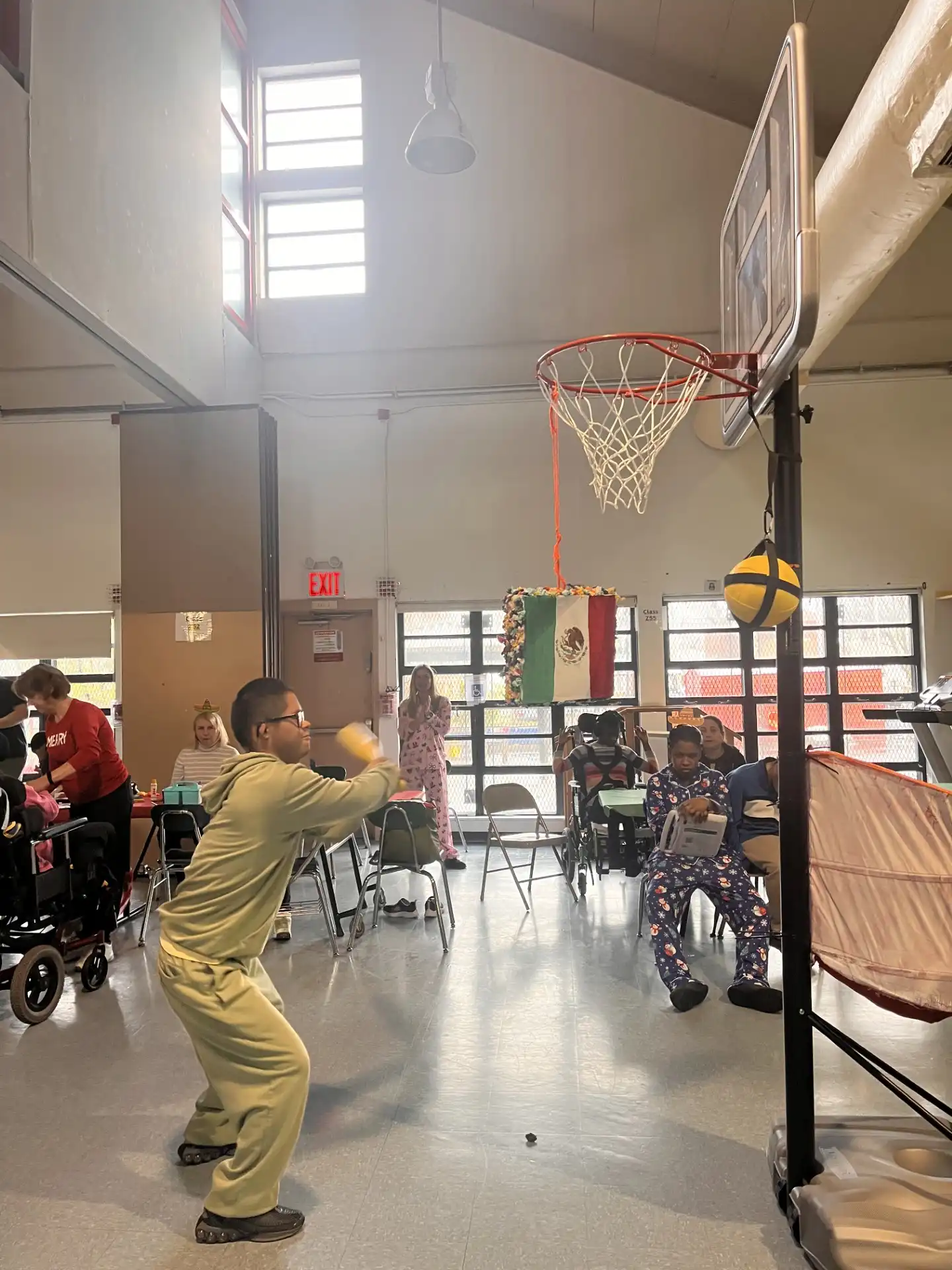 A student playing a piñata game with a piñata hanging from a basketball rim during a school celebration