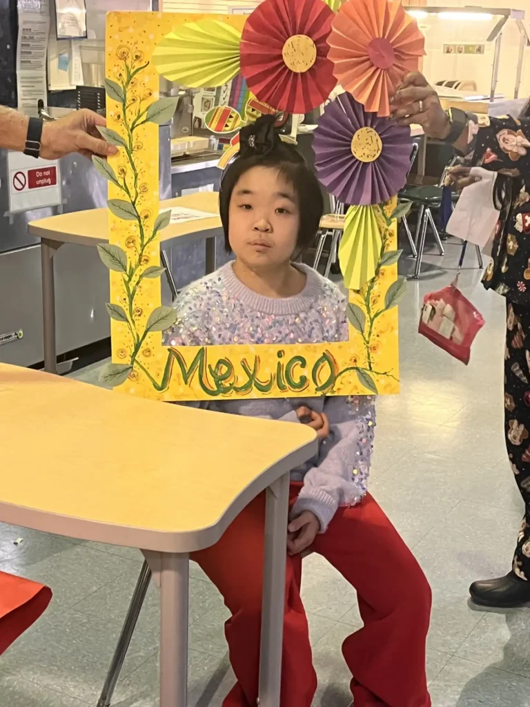 A student holding a festive, flower-decorated 'Mexico' photo frame during a school cultural celebration