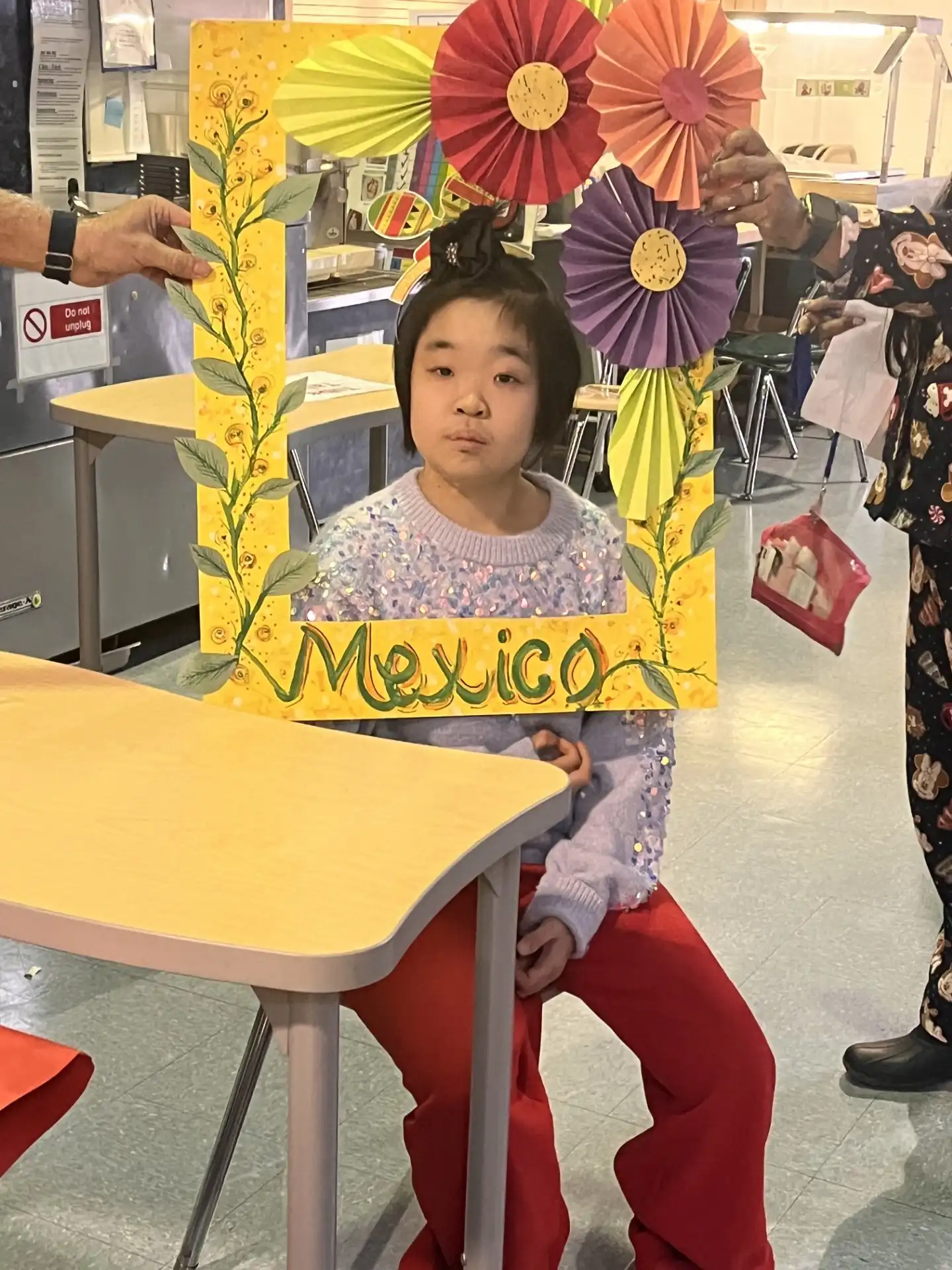 A student holding a festive, flower-decorated 'Mexico' photo frame during a school cultural celebration