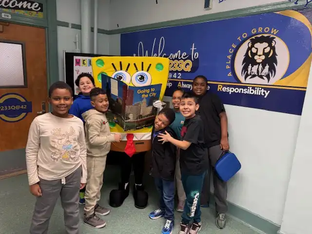 Mascot character SpongeBob SquarePants reading a story to a captivated group of elementary school students during a literacy event."