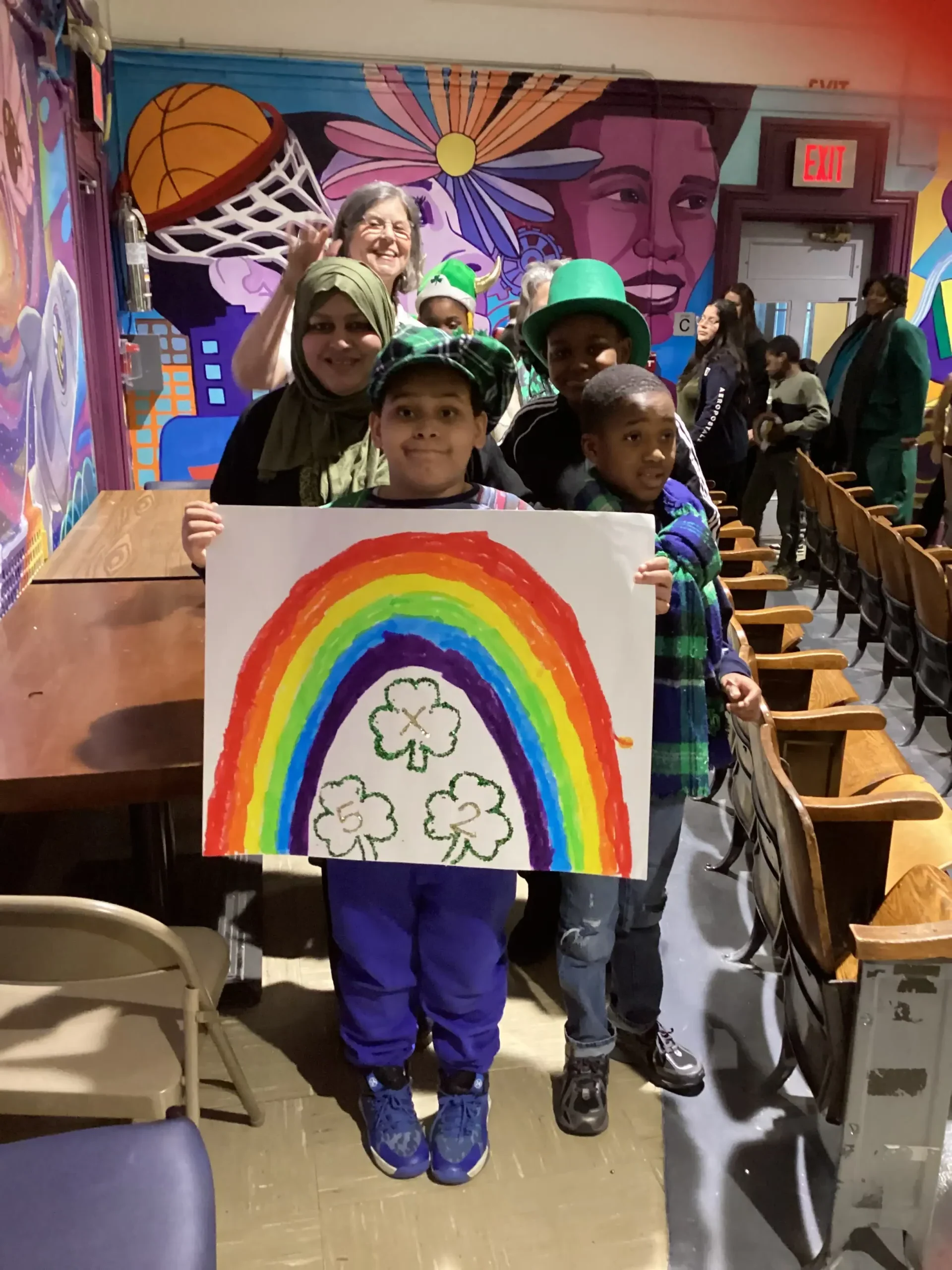 four students dressed in green and festive St. Patrick’s Day colors, smiling and holding a holiday-themed sign.